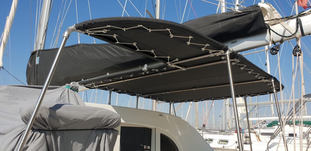 Taud bimini sur-mesure noir avec structure inox et lazy bag pour voile, installé sur un voilier de plaisance dans un port